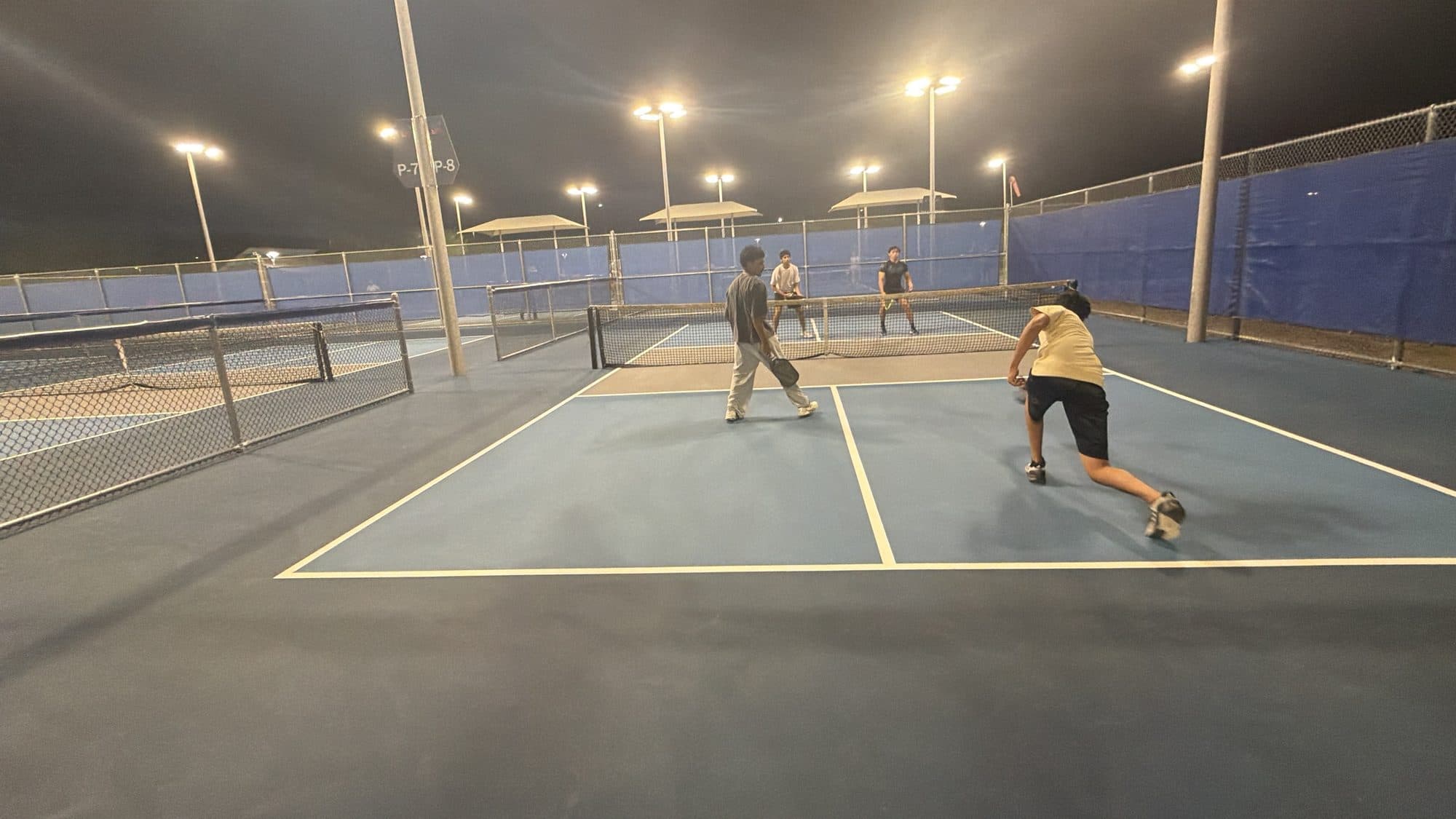 A player lunging low to dig out a shot while three others hold position on court