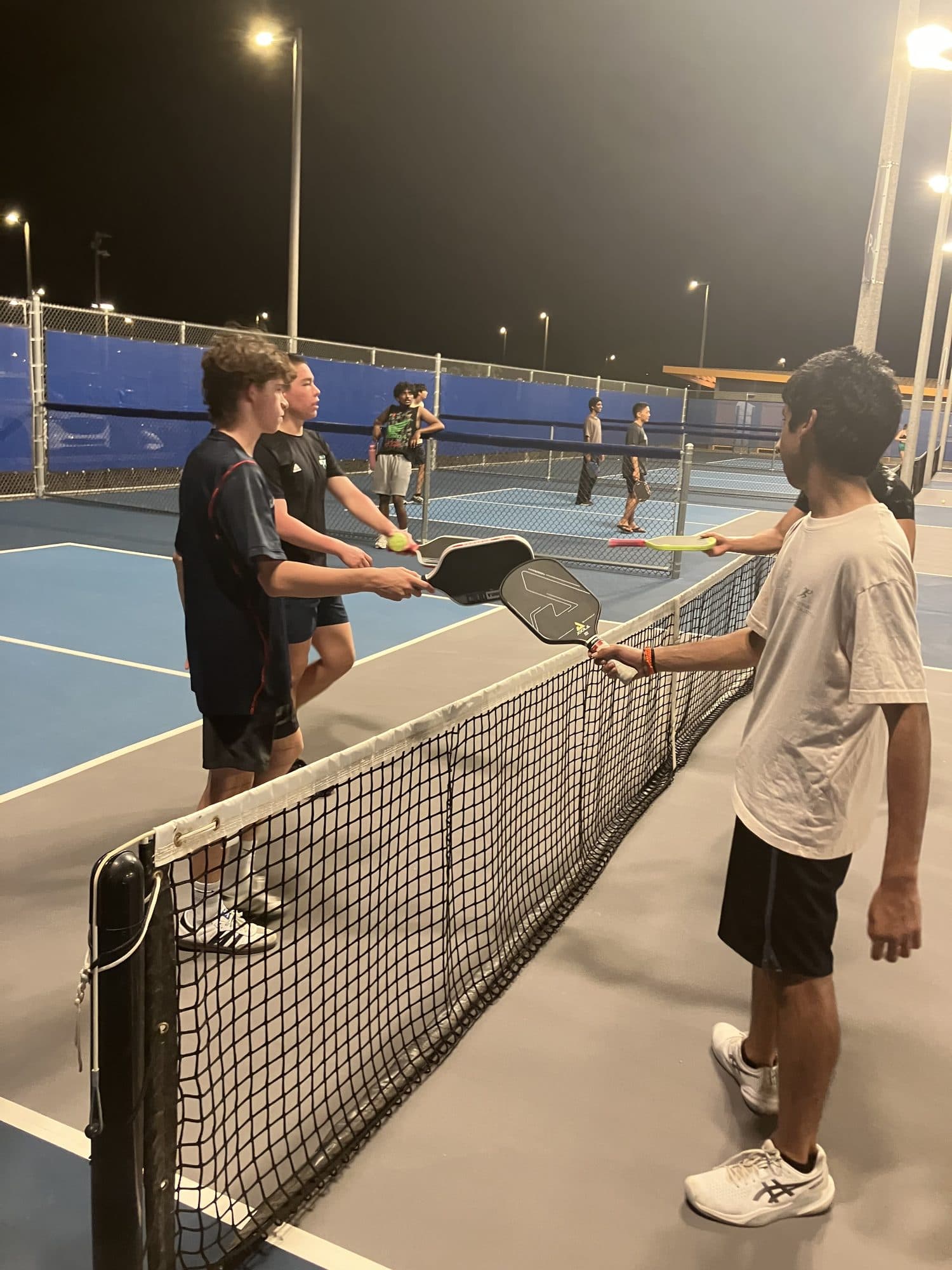 Players meeting at the net with paddles raised during a doubles match under the court lights