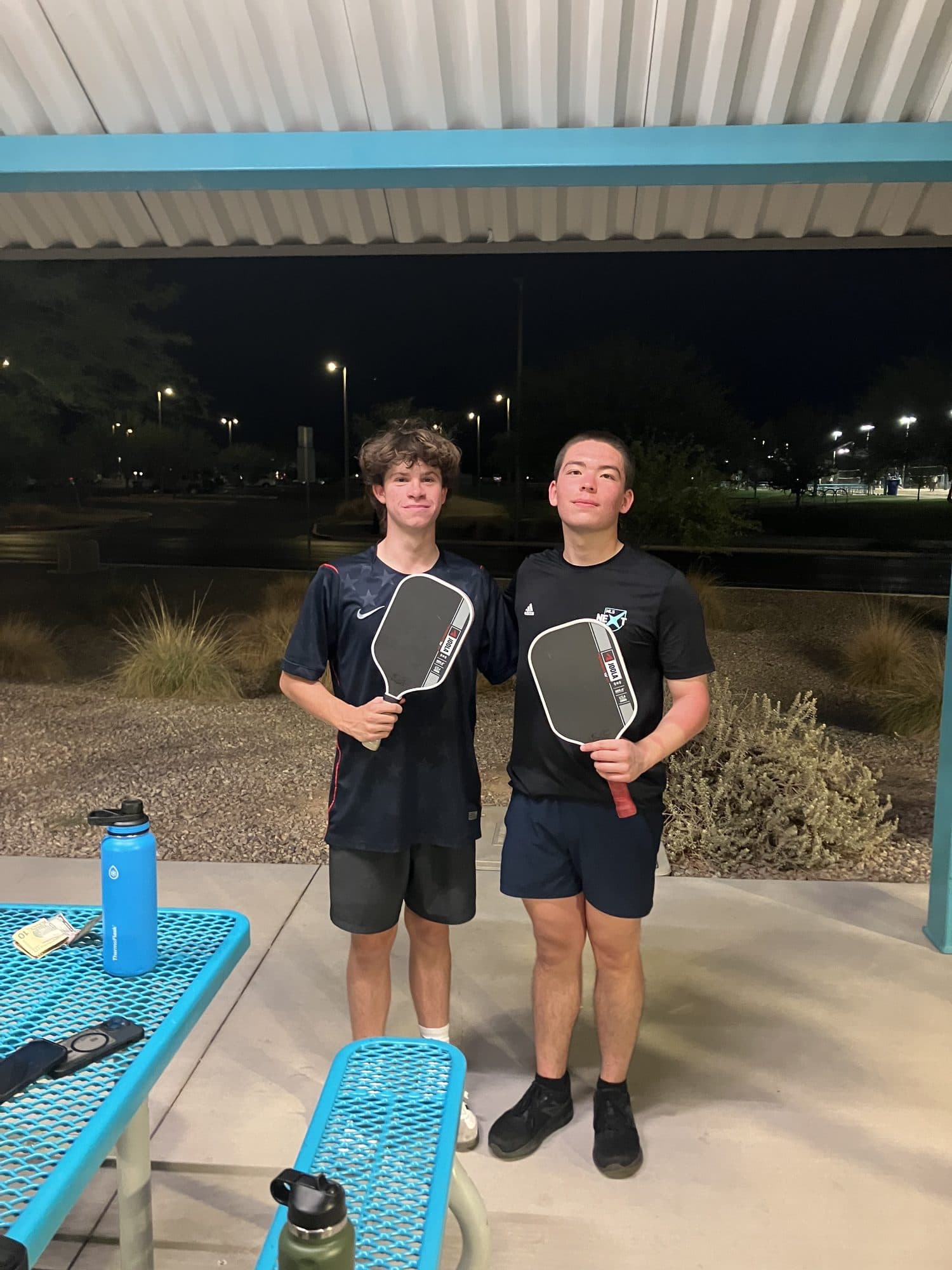 Two players standing together with their paddles under the park ramada at the end of the night