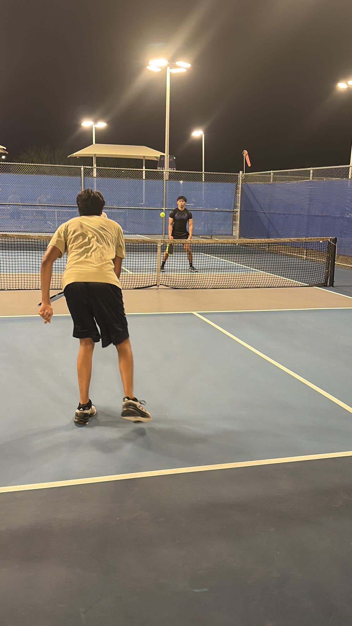 A player in a ready stance at the baseline waiting on the serve, opponent visible across the net